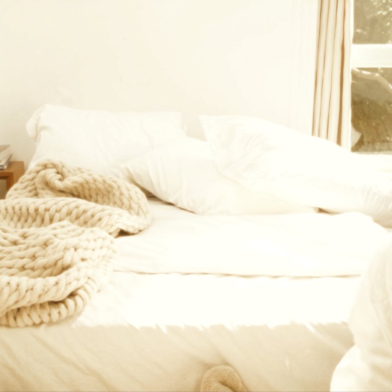 A cozy bed with a knit blanket in morning light